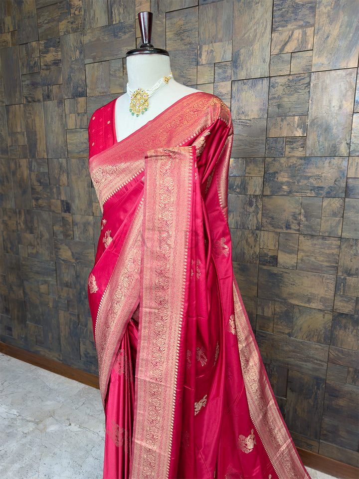 Red saree with gold patterns on a mannequin against a textured wall. Close-up view of the House of Vardha Crimson Red Satin Saree highlighting the detailed Light Gold Zari floral motifs and the precision of the woven border. We offer Ready to wear, Pre drape service, Saree Add on, Custom Stitched Blouse, Fall and Edging, Gift Packaging at Complimentary Price!