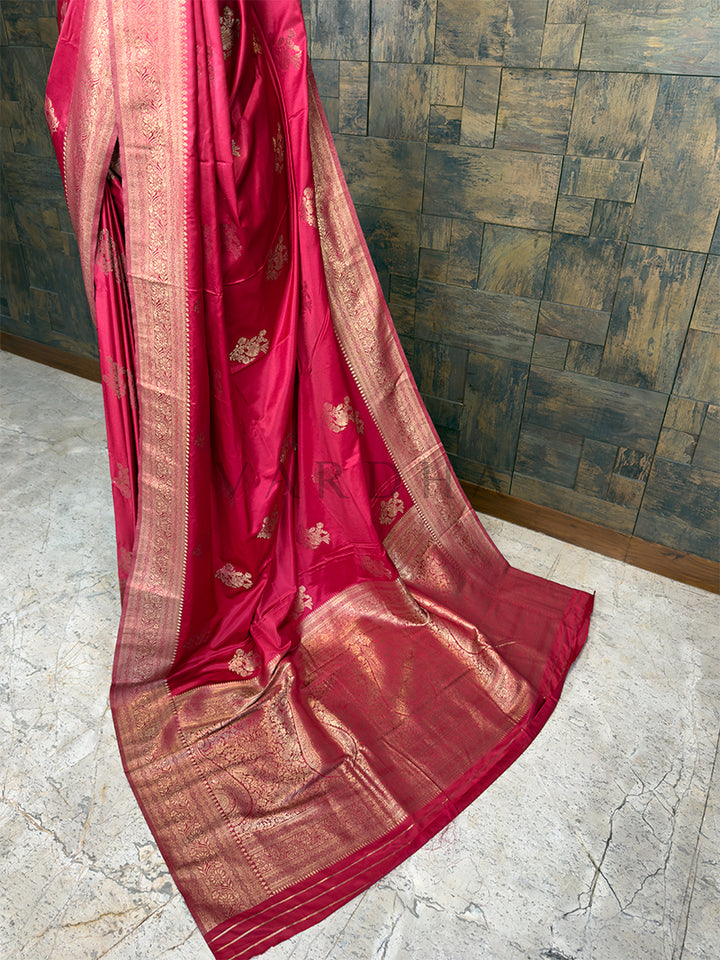 Red saree with gold patterns on a stone floor and tiled wall background. Elegant Crimson Red festive satin saree from House of Vardha with radiant Light Gold Zari work, perfect for weddings, parties, and special occasions. We offer Ready to wear, Pre drape service, Saree Add on, Custom Stitched Blouse, Fall and Edging, Gift Packaging at Complimentary Price! House of Vardha designer Crimson Red Satin Saree featuring traditional Light Gold Zari buttis across the body and a decorative pallu. We offer Ready to 