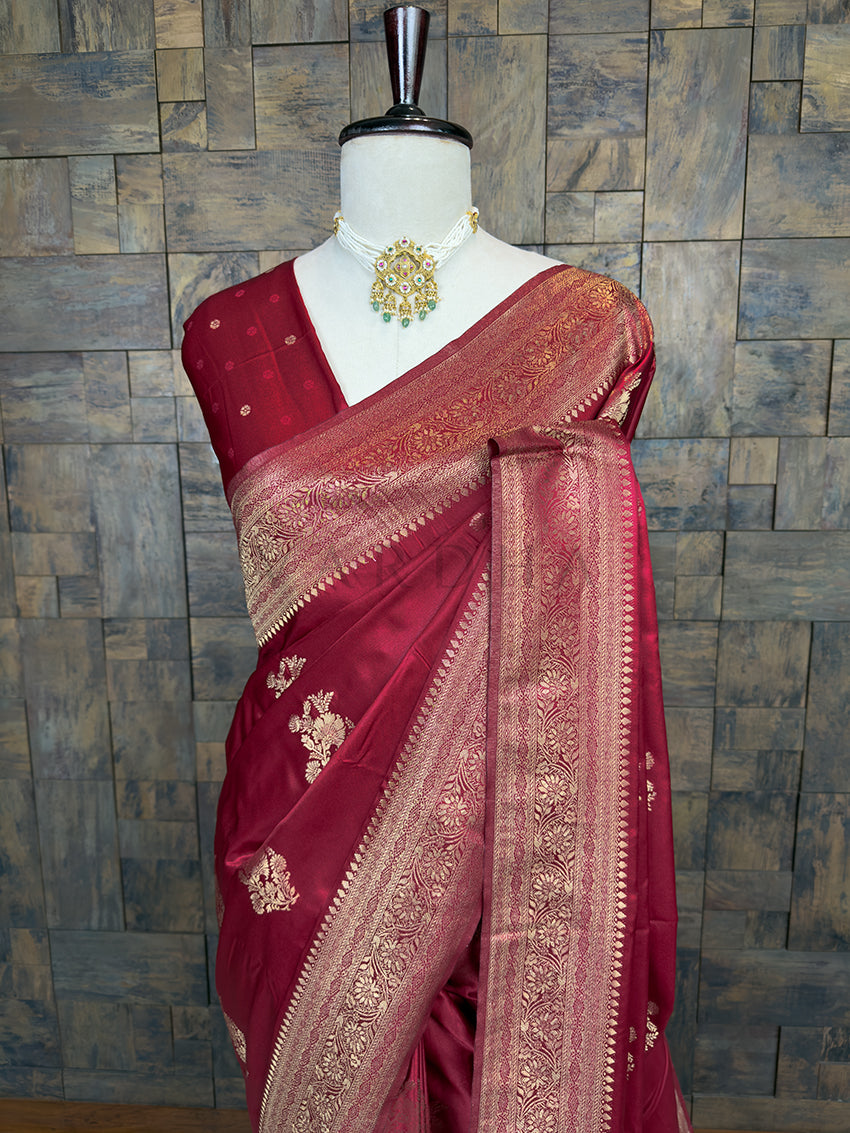 Maroon saree with gold patterns on a mannequin against a wooden paneled wall. Lustrous Deep Maroon Satin Saree by House of Vardha showcasing intricate Gold Zari floral weaving and a rich, smooth texture. We offer Ready to wear, Pre drape service, Saree Add on, Custom Stitched Blouse, Fall and Edging, Gift Packaging at Complimentary Price!