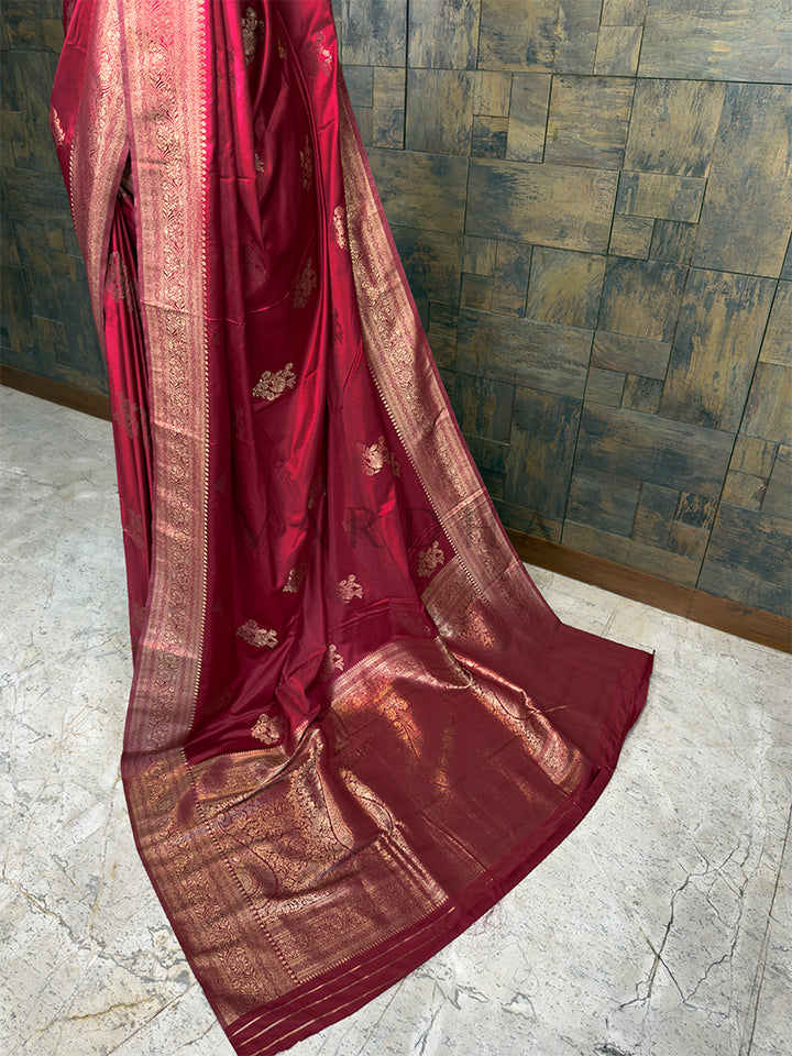 Red saree with gold patterns on a textured wall background. Elegant Deep Maroon festive satin saree from House of Vardha with radiant Gold Zari work, perfect for Indian weddings and special occasions. We offer Ready to wear, Pre drape service, Saree Add on, Custom Stitched Blouse, Fall and Edging, Gift Packaging at Complimentary Price! House of Vardha designer Deep Maroon Satin Saree featuring traditional Gold Zari floral buttis across the body and a decorative pallu. We offer Ready to wear, Pre drape servi
