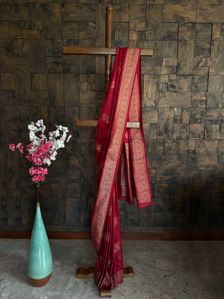 Deep cherry red satin saree with copper zari woven floral border and pallu. Beautifully draped Deep Maroon Satin Saree showcasing the soft fall of the fabric and the glimmer of the Gold Zari floral patterns by House of Vardha. We offer Ready to wear, Pre drape service, Saree Add on, Custom Stitched Blouse, Fall and Edging, Gift Packaging at Complimentary Price!
