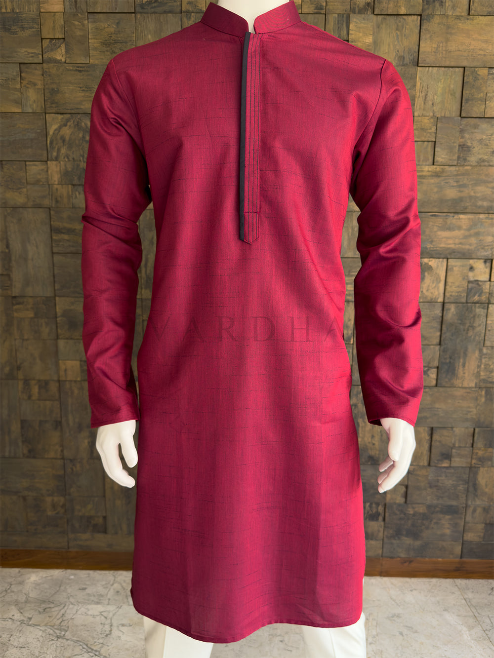 Maroon kurta on a mannequin against a wooden paneled wall. Close-up of the burgundy red men's festive kurta showcasing the fine horizontal slub cotton texture and a striking dark contrast center placket for a clean minimalist look.