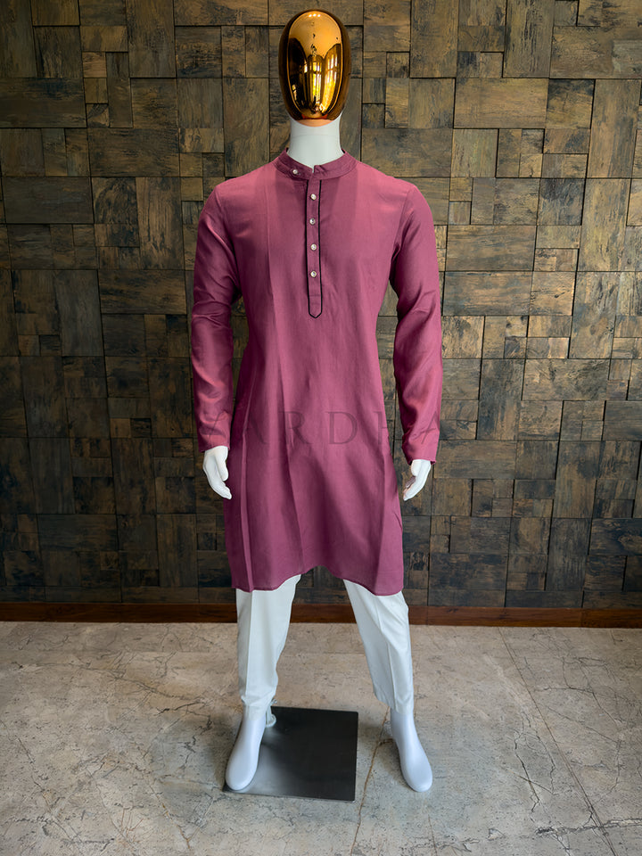 Mannequin wearing a maroon kurta with white pants against a wooden paneled wall. Front view of a man wearing a deep mauve pink cotton kurta with a dark contrast piped placket.