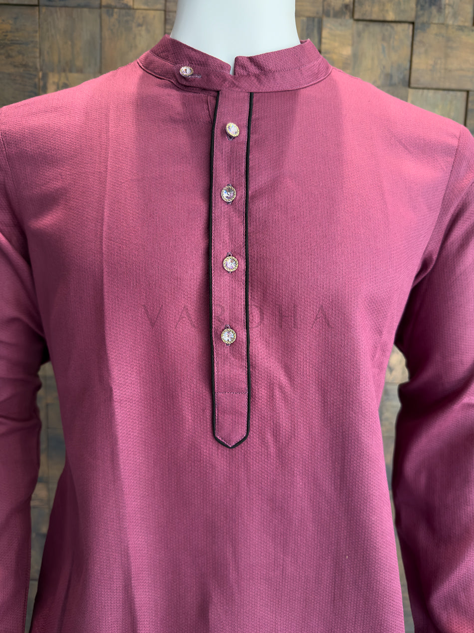 Mauve kurta on a mannequin against a stone wall background Detailed view of the dark contrast piping and crystal-studded designer buttons on the pink kurta.