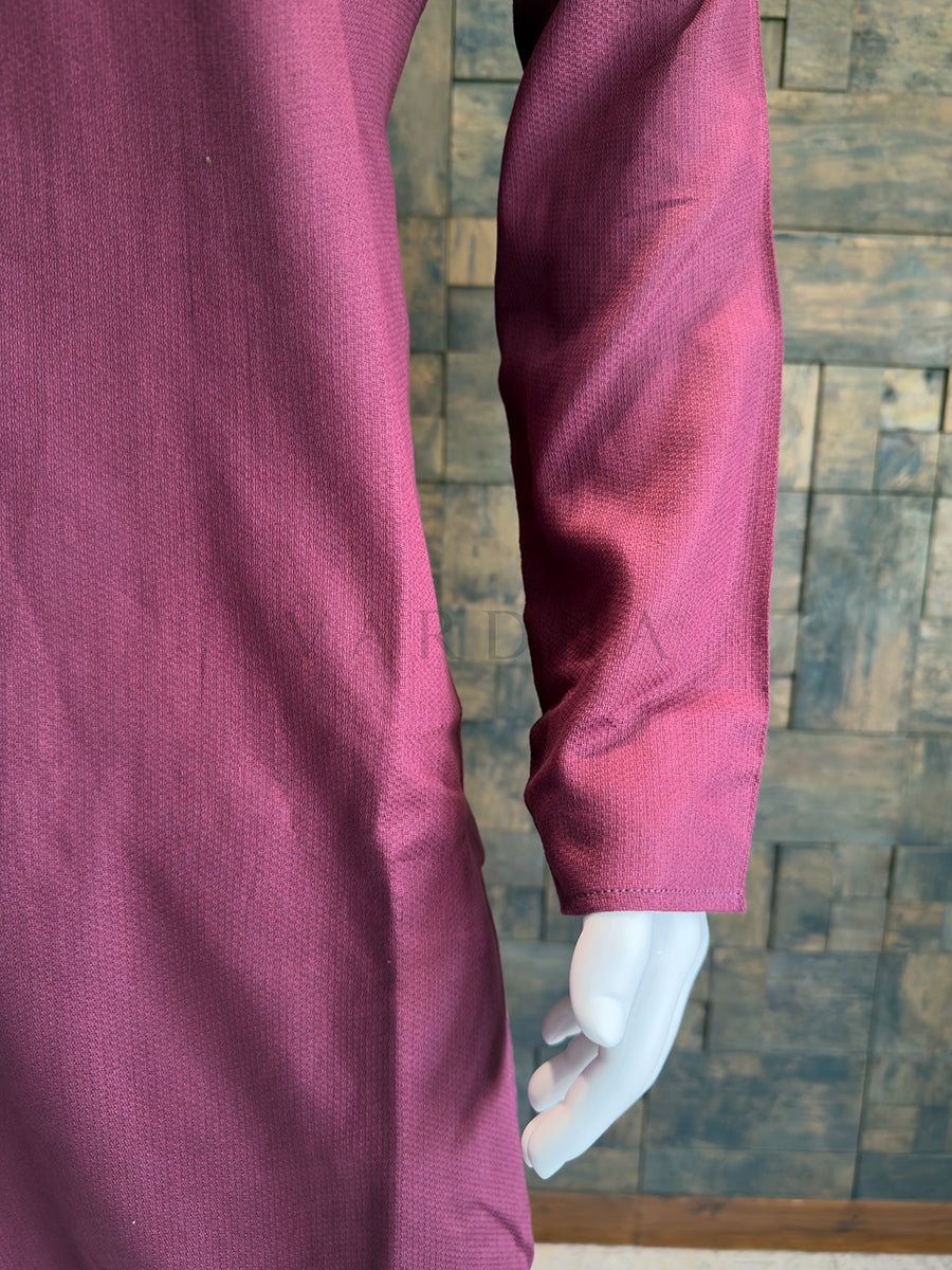 Close-up of a maroon garment with long sleeves against a wooden paneled wall. Close-up of the full sleeve and subtle woven slub texture on the deep mauve pink cotton kurta.