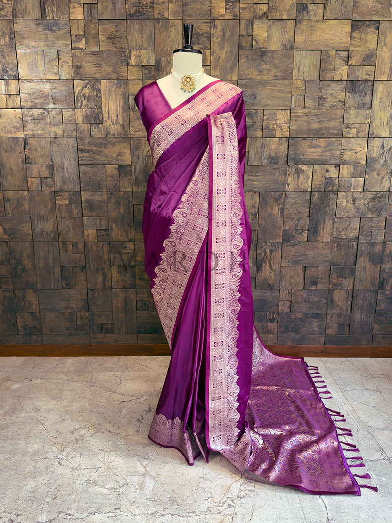 Purple saree with white border on a mannequin against a wooden paneled wall. Full front display of a solid deep purple satin silk saree featuring a heavy golden zari border draped gracefully on a mannequin.
