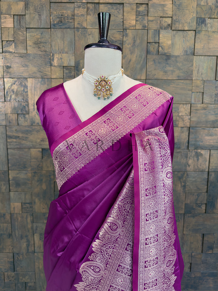 Purple saree with white patterns on a mannequin against a stone wall background Close-up of a deep purple woven satin ethnic saree styled on a mannequin display, paired with a traditional pearl choker necklace.