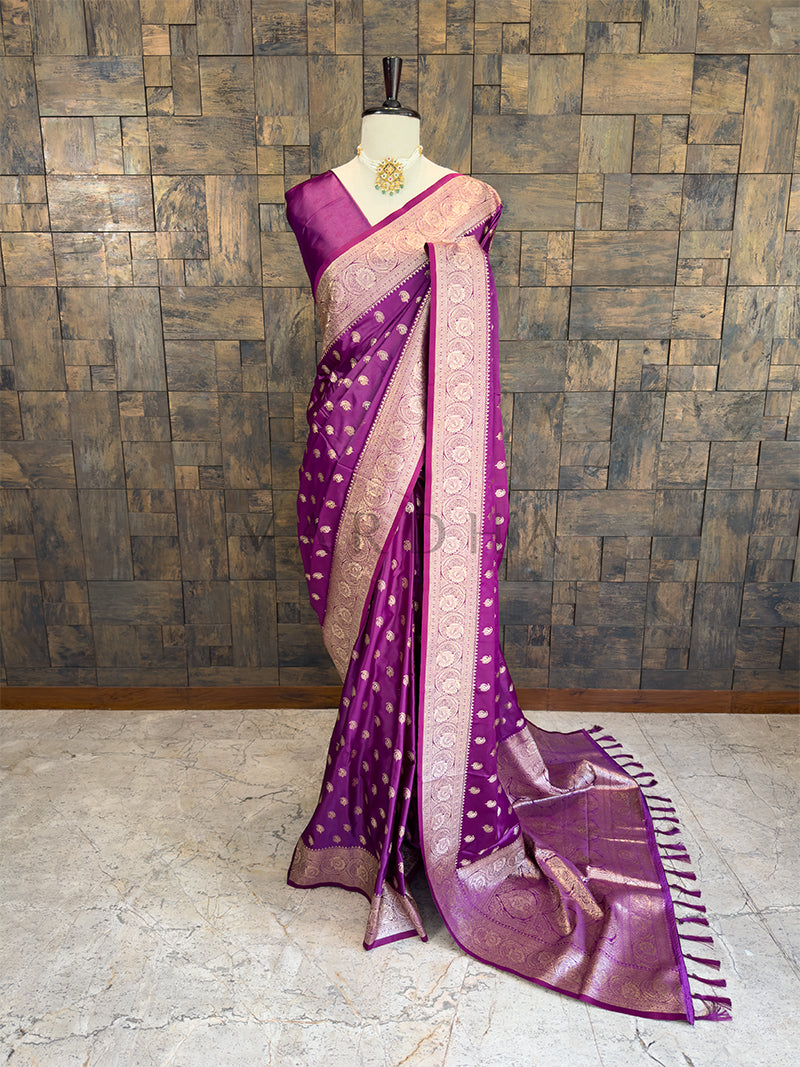 Purple and beige saree on a mannequin against a textured wall. Full front display of a deep purple satin silk saree featuring golden zari paisley bootis draped gracefully on a mannequin.