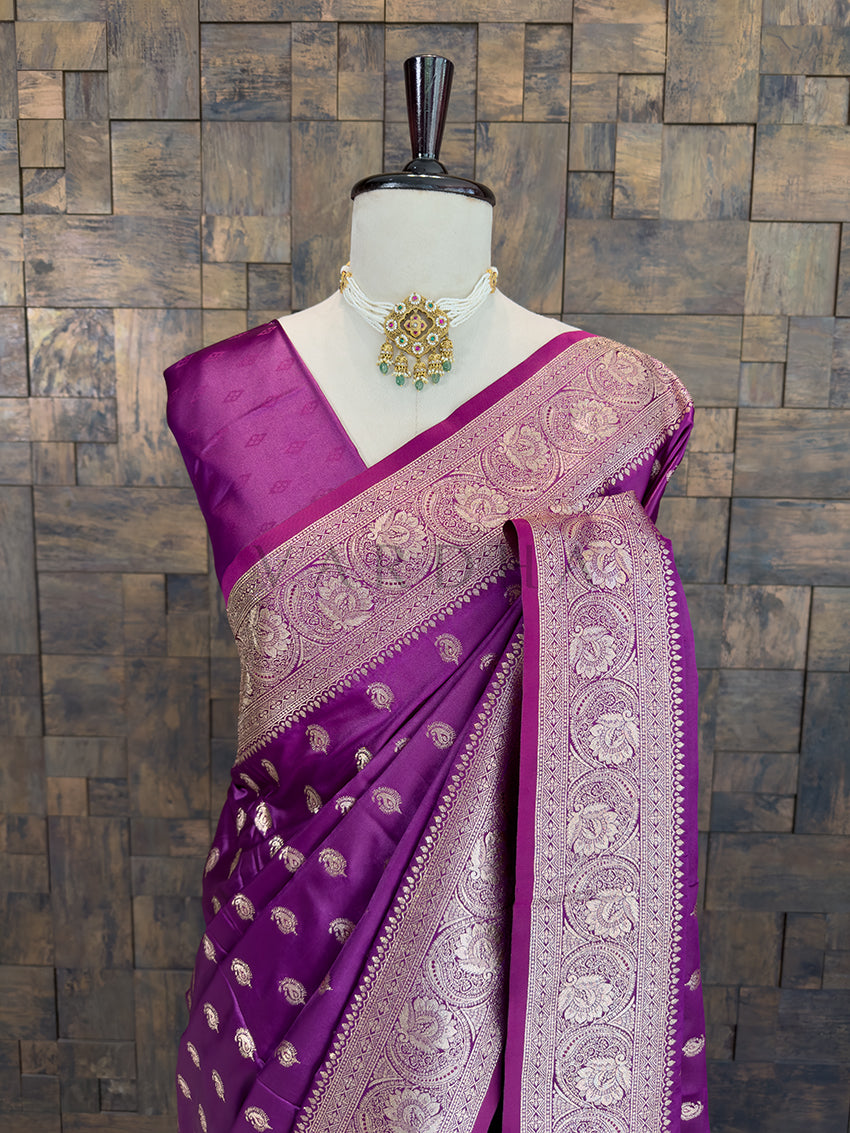 Purple saree with gold patterns on a mannequin against a wooden paneled wall. Close-up of a rich purple woven satin ethnic saree styled on a mannequin display, paired with a traditional pearl choker necklace.