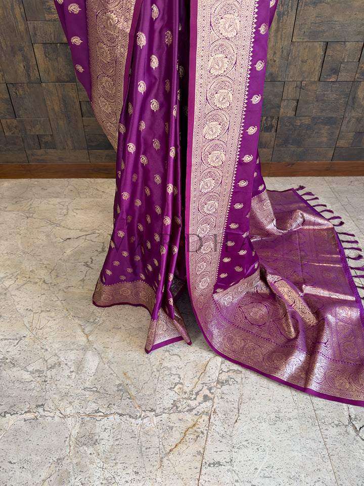 Purple saree with gold patterns on a stone floor Lower pleats and fluid drape of a glossy plum Banarasi-style satin silk saree showcasing the broad circular floral border.