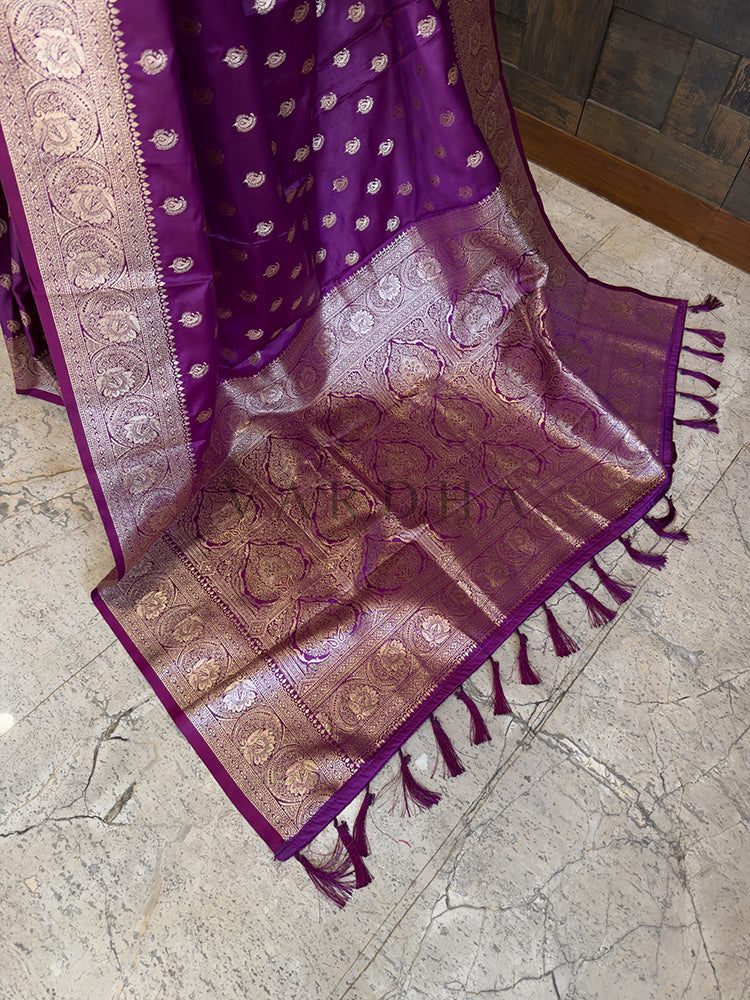 Purple and brown saree with intricate patterns on a marble floor Detailed floor view of the rich, densely woven golden zari pallu with matching tassels on a vibrant deep purple satin saree.