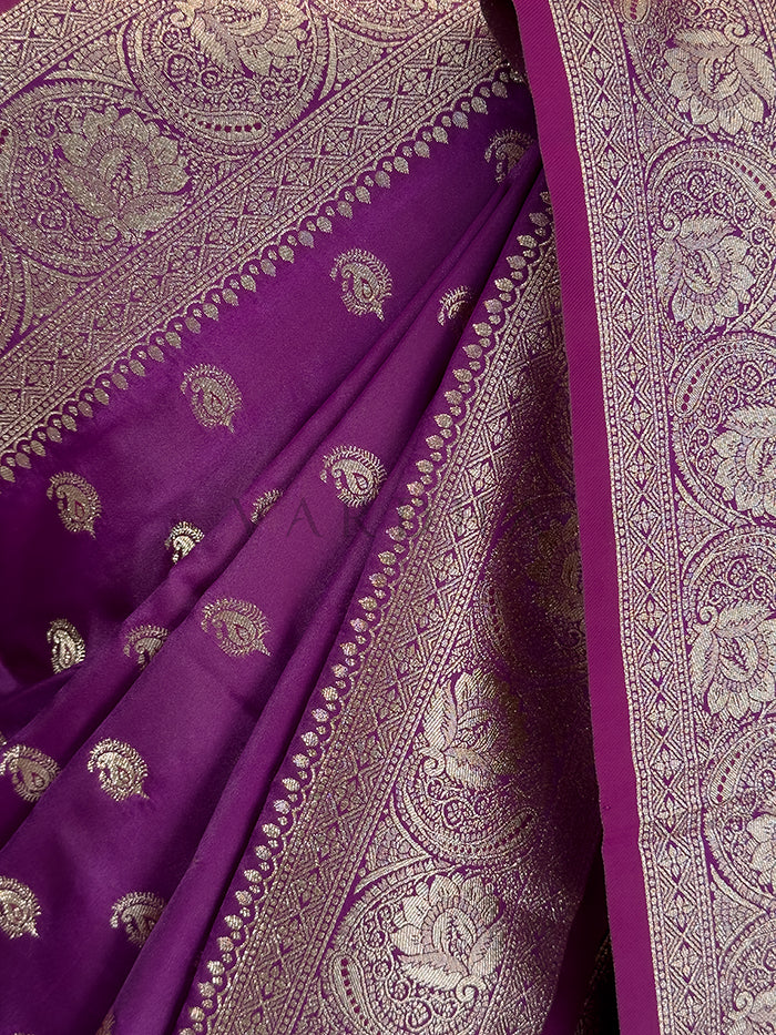 Purple fabric with intricate white patterns  Close-up texture shot highlighting the woven paisley bootis and dense traditional zari border on a deep purple satin fabric. Rich Indian wedding guest attire featuring a deep purple satin saree with opulent paisley border details and traditional metallic weaving. Festive ethnic wear deep purple zari woven saree sweeping the floor, showcasing the heavily brocaded pallu and traditional patterns. Elegant party wear plum satin silk saree highlighting its smooth drape