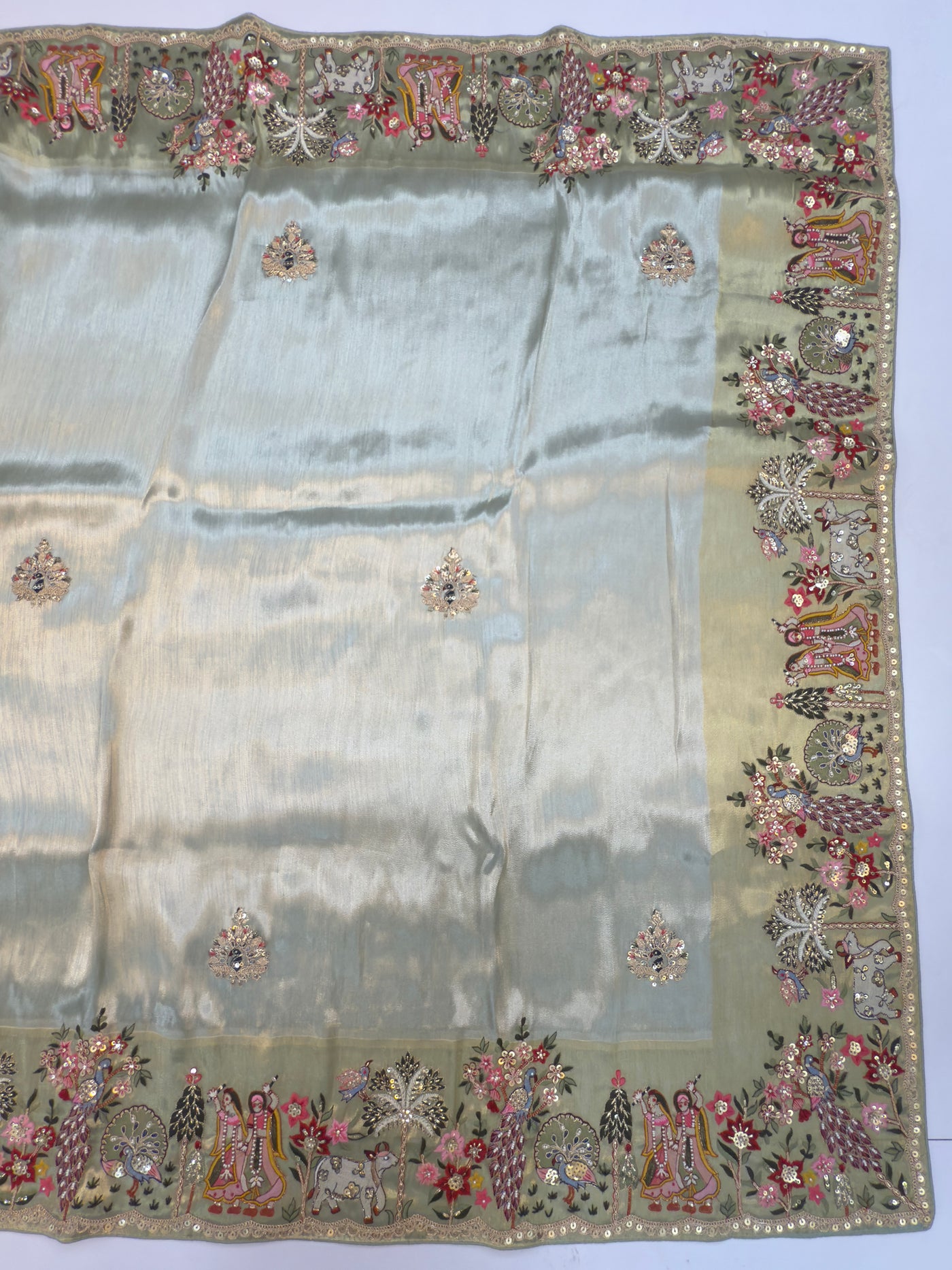Folded presentation showing intricate Radha Krishna and peacock motif embroidery in vibrant, detailed fashion for bridal occasions.

