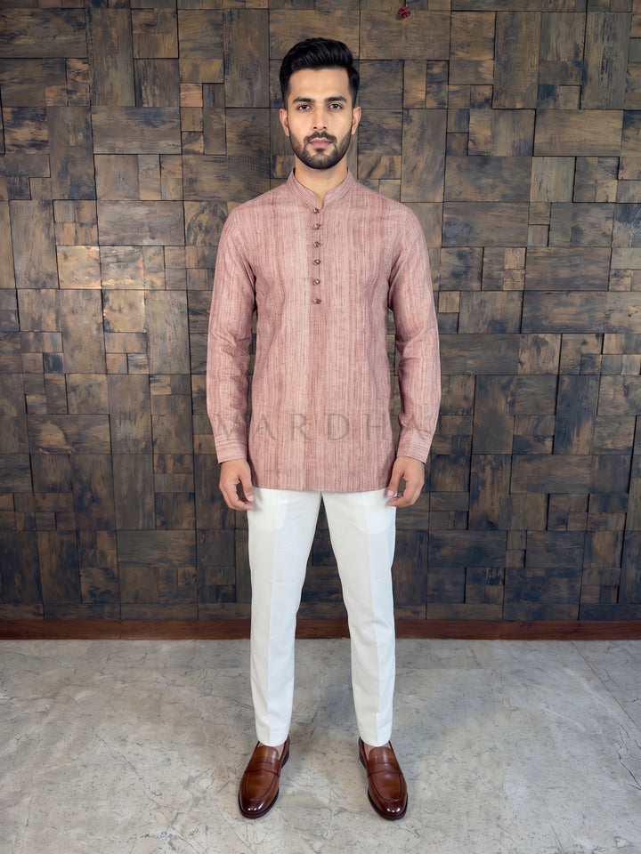 Man wearing a pink kurta with white pants against a wooden paneled wall.