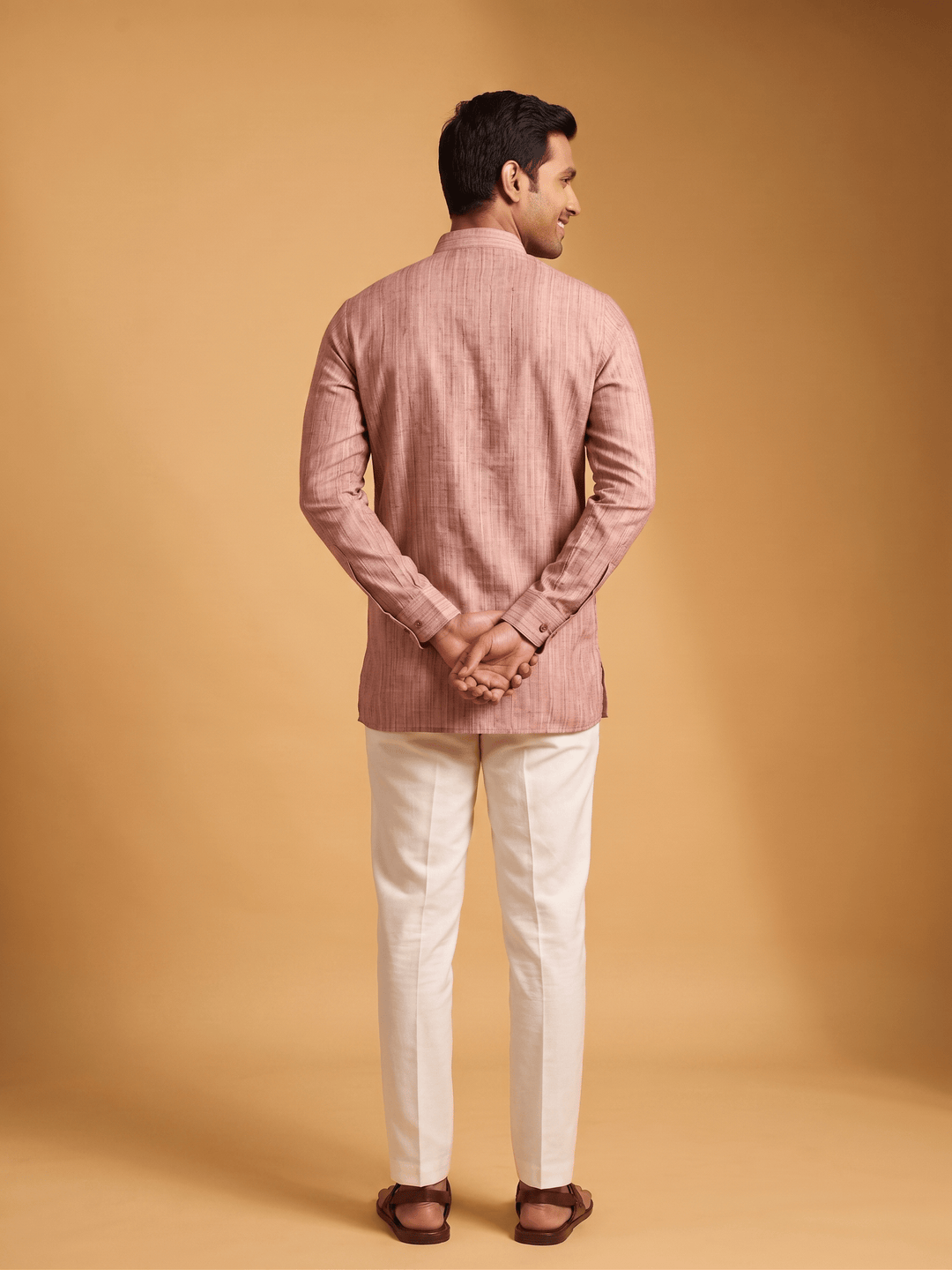 Back view of a man wearing a dusty cedar textured cotton short kurta with white trousers.