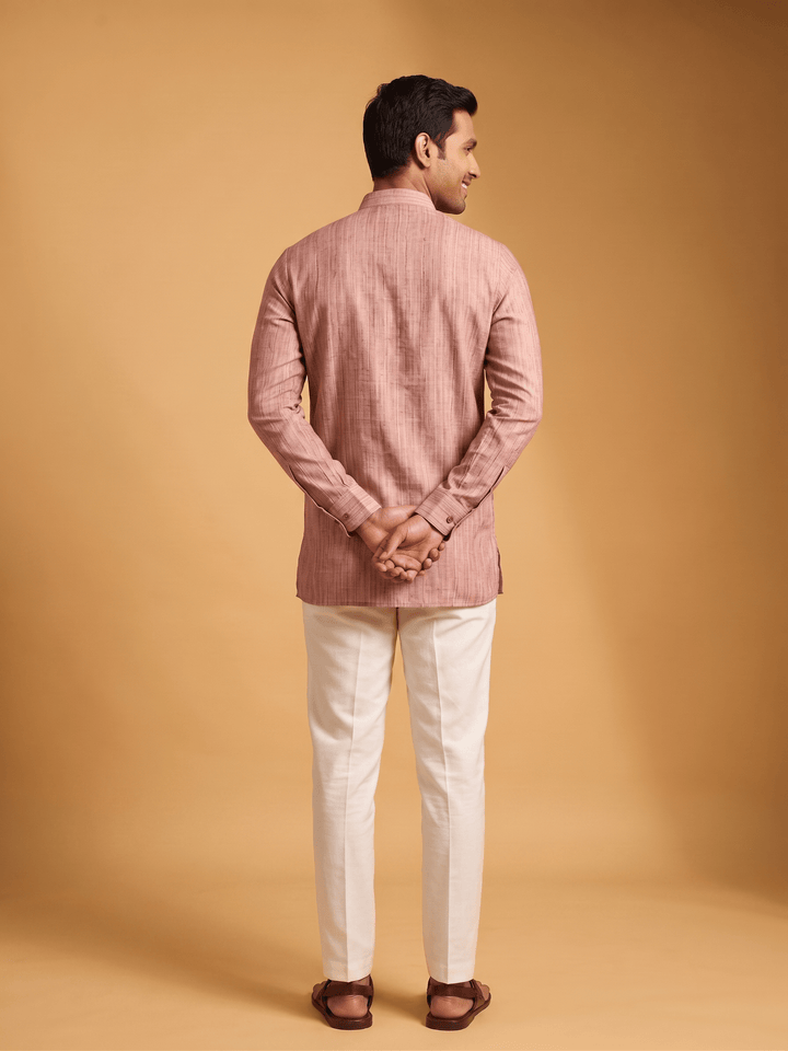Back view of a man wearing a dusty cedar textured cotton short kurta with white trousers.