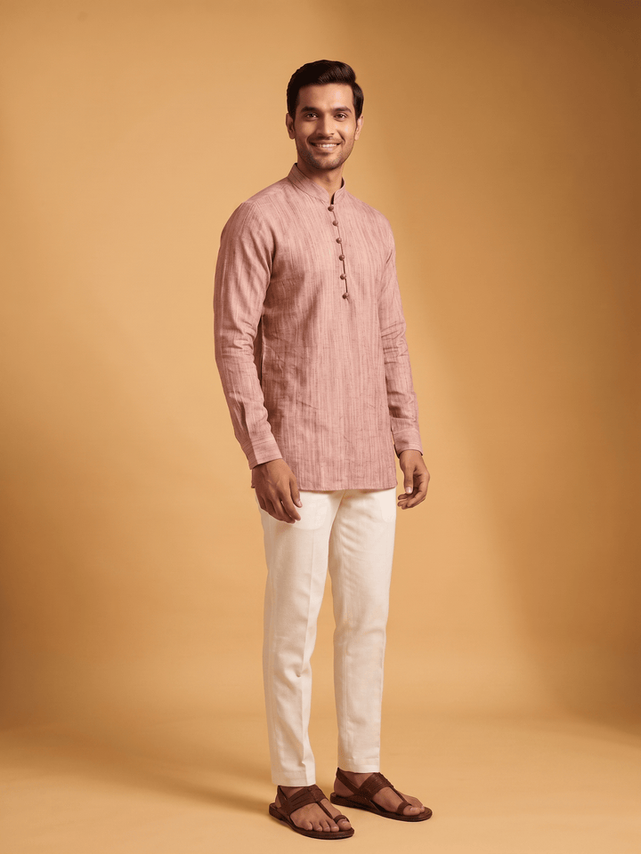 A man standing in a dusty cedar textured cotton short kurta paired with white trousers, relaxed pose.