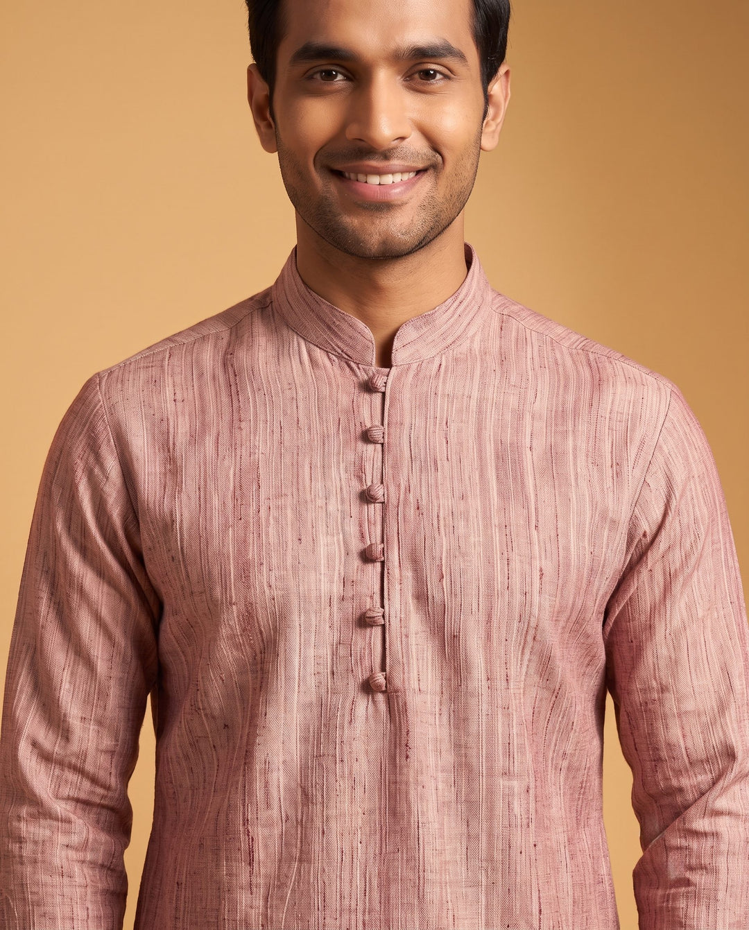 A man wearing a dusty rose pink kurta with a textured vertical stripe pattern, standing against a solid warm beige background. Medium close-up view of a man wearing a dusty cedar textured cotton short kurta, focus on fabric texture and neckline.