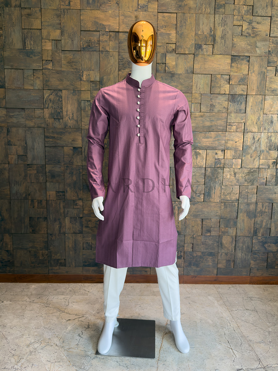 Mannequin wearing a mauve kurta against a wooden paneled wall. Sophisticated Dusty Mauve Pink kurta for men, blending a contemporary pastel palette with sharp architectural tailoring and a Mandarin collar.
