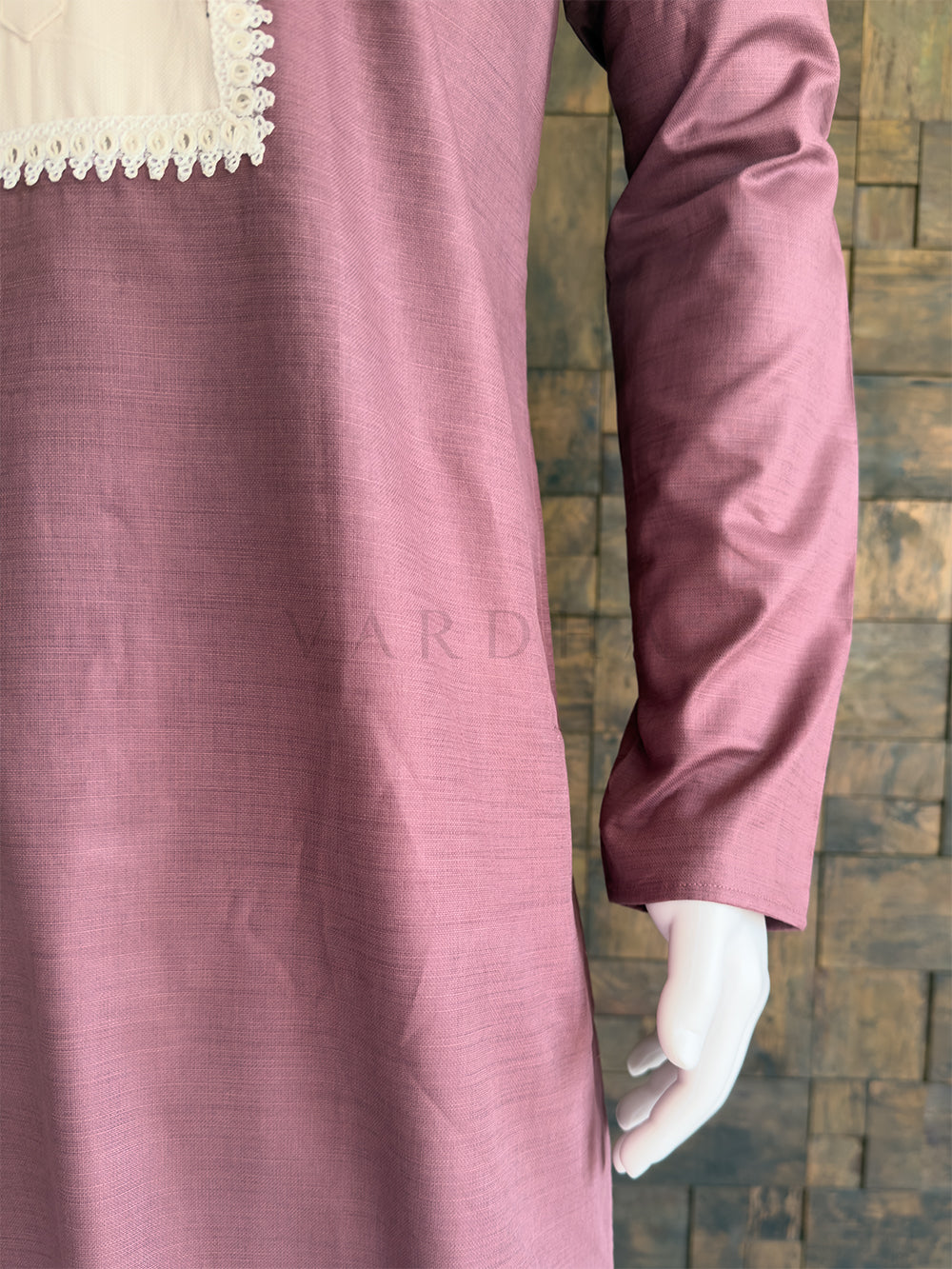 Close-up of a mauve long-sleeve top with lace trim on a textured wall background. Side angle of the beautifully tailored pink cotton kurta for men, highlighting the striking contrast yoke design and mandarin collar for traditional celebrations.