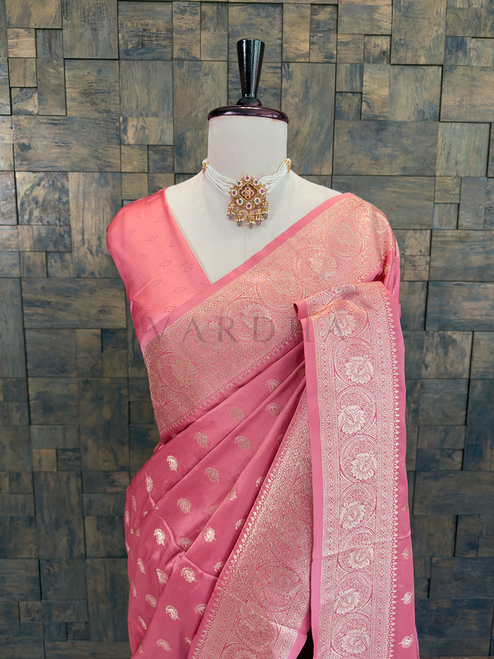 Pink saree with intricate patterns on a mannequin against a textured wall. Close-up of a soft peach-pink woven satin ethnic saree styled on a mannequin display, paired with a traditional pearl choker necklace. Festive ethnic wear dusty rose zari woven saree sweeping the floor, showcasing the heavily brocaded pallu and traditional patterns.