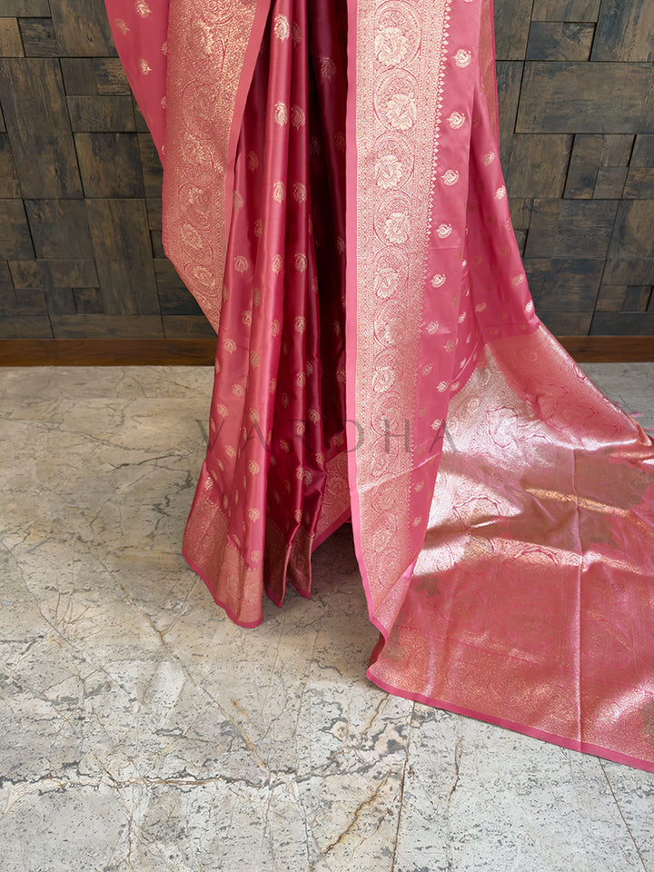 Pink saree with gold patterns on a stone floor and wooden wall background Lower pleats and fluid drape of a glossy dusty pink Banarasi-style satin silk saree showcasing the broad circular floral border.