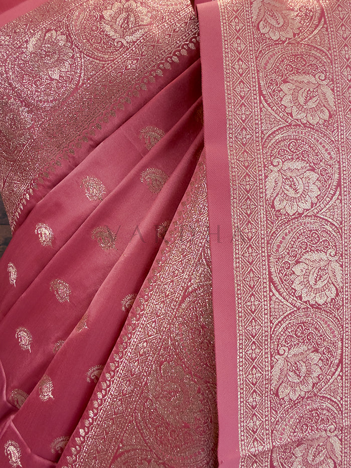 Pink saree with intricate white patterns on a plain background Close-up texture shot highlighting the woven paisley bootis and dense traditional zari border on a dusty rose pink satin fabric. Rich Indian wedding guest attire featuring a peach-pink satin saree with opulent paisley border details and traditional metallic weaving.
