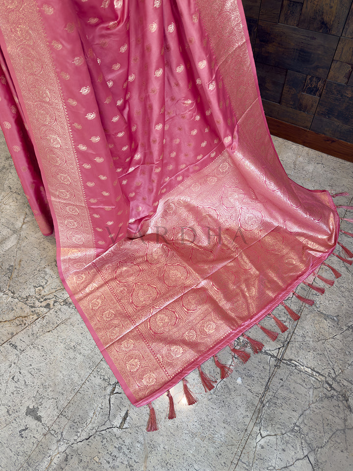 Pink saree with intricate patterns on a textured floor Detailed floor view of the rich, densely woven golden zari pallu with matching tassels on an elegant dusty rose satin saree.