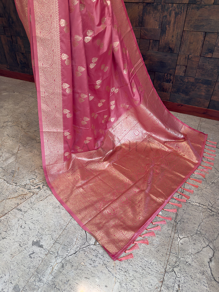 Pink saree with a textured pattern on a stone floor and wooden wall Lower pleats and fluid drape of a glossy blush pink Banarasi-style satin silk saree with a heavy zari border.background Detailed floor view of the rich, heavy golden zari woven pallu with matching tassels on the luxurious rose pink satin saree.