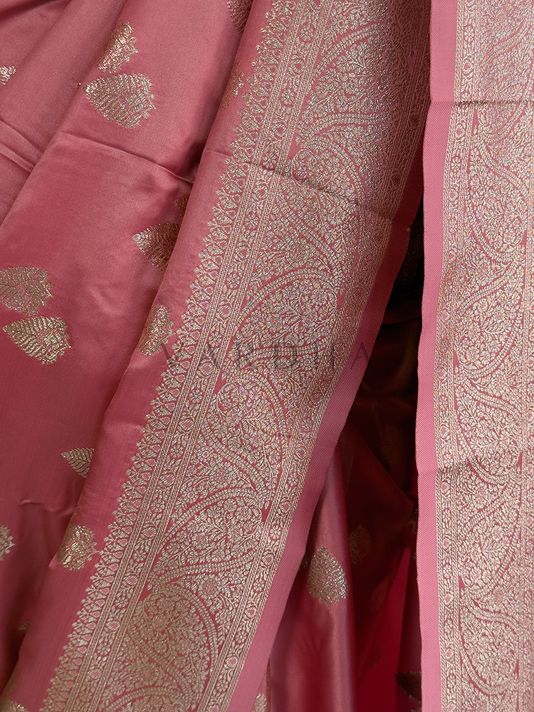 Close-up of a pink fabric with intricate gold patterns Festive ethnic wear light pink zari woven saree sweeping the floor, showcasing the heavily brocaded pallu and traditional patterns. Rich Indian wedding guest attire featuring a soft dusty rose satin saree with opulent paisley pallu details and a woven border.