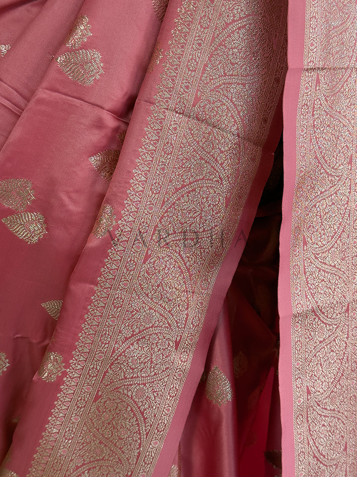 Close-up of a pink fabric with intricate gold patterns Festive ethnic wear light pink zari woven saree sweeping the floor, showcasing the heavily brocaded pallu and traditional patterns. Rich Indian wedding guest attire featuring a soft dusty rose satin saree with opulent paisley pallu details and a woven border.