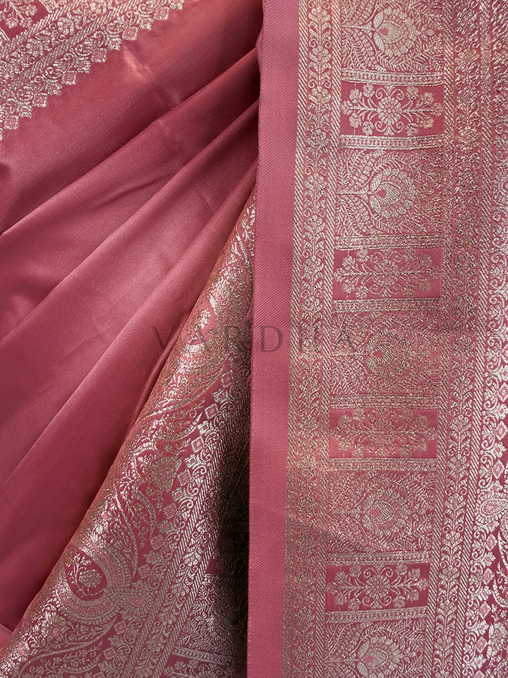Pink fabric with intricate silver patterns Close-up texture shot highlighting the solid glossy pink fabric contrasting with the intricate geometric floral zari border. Rich Indian wedding guest attire featuring a solid dusty pink satin saree with opulent border details and traditional metallic weaving.
