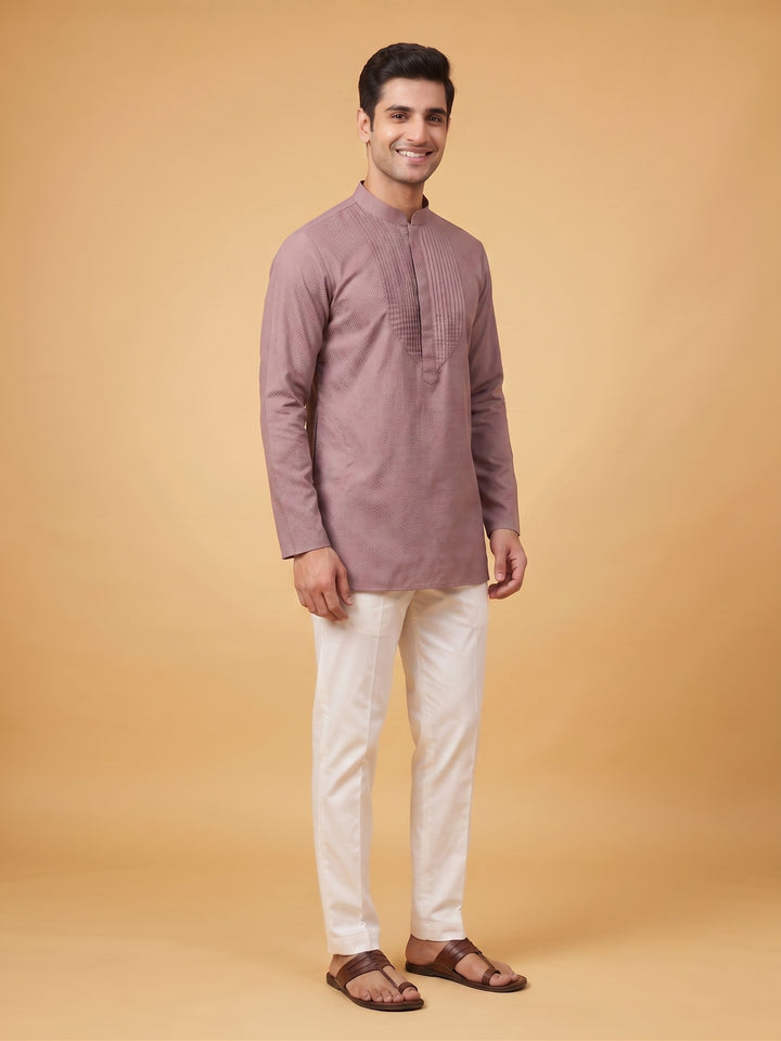 A man standing in a dusty taupe cotton short kurta with a structured pintuck yoke, posing in a smart casual style.