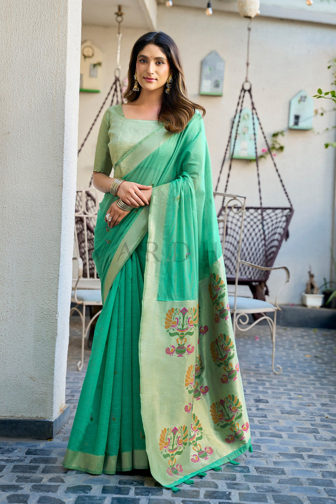 Woman wearing a green saree with floral patterns in an outdoor setting Emerald Green Cotton Jacquard Saree with Paithani Pallu &amp; Zari Border