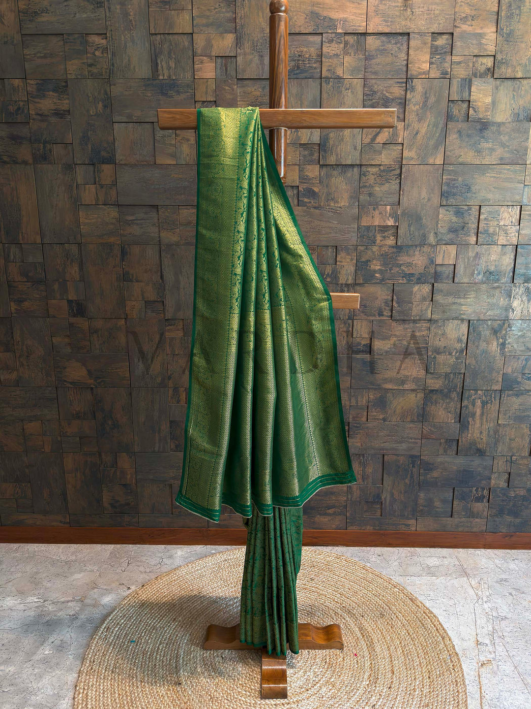 Emerald green Kanjivaram art silk saree on stand with golden zari floral jaal and geometric brocade borders, full drape view showing rich pallu and structured pleats traditional festive Indian saree.