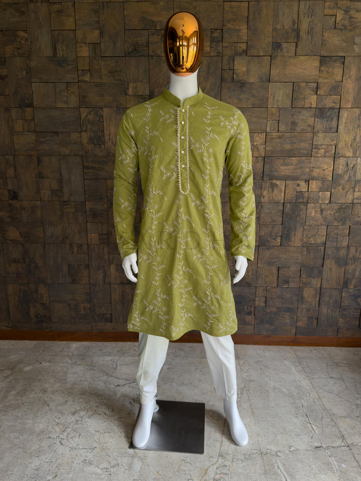 Mannequin wearing a green kurta with white patterns against a wooden paneled wall. Front view of a man wearing a regal emerald green viscose kurta featuring all-over floral vine embroidery. This is an incredibly rich, regal Emerald Green Deep Bottle Green long kurta. Dark, jewel-toned greens are traditional favorites for evening celebrations, making this piece an ideal anchor for Sangeet nights, Mehendi events, and formal wedding receptions.