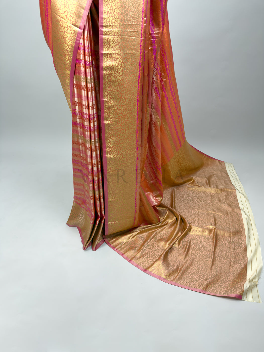 A side-view and full-length perspective focusing on the front pleats of the draped Off White Tanchoi Silk Saree. It showcases the vertical bands of intricate gold Tanchoi weaving patterns. The detailed pallu flows to the side with elaborate threadwork, and the distinct striped cream tail end of the pallu drapes elegantly on the floor, displaying the saree&