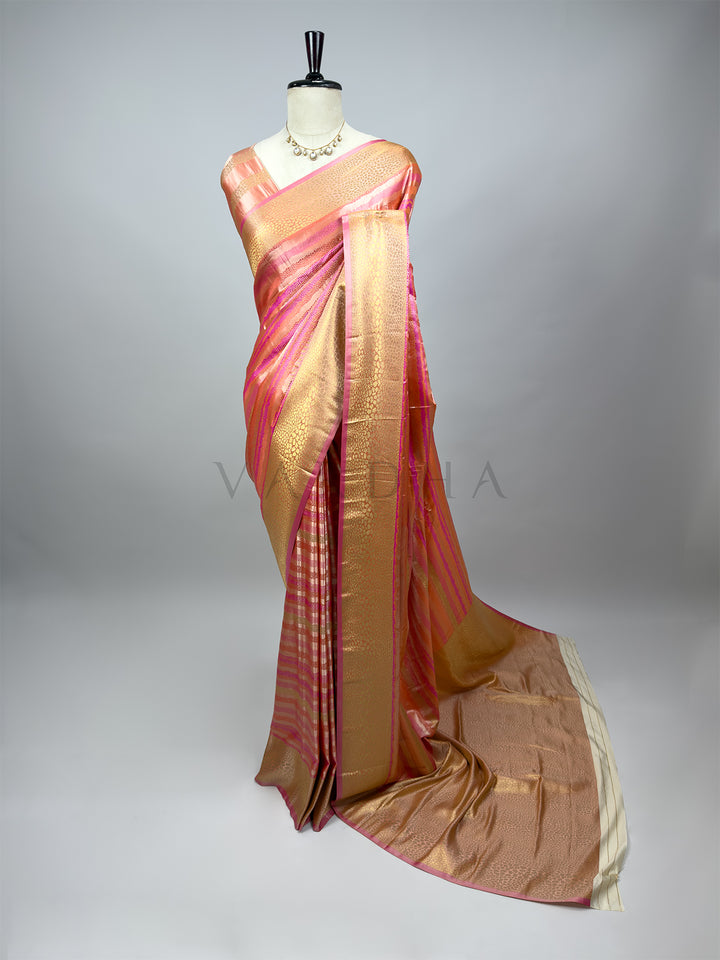 A full-length drape of an Exquisite Off White Tanchoi Silk Saree (Visually: Peach and Gold) on a mannequin with a delicate kundan necklace. The saree features intricate thread weaving of dense gold and cream floral and paisley patterns on alternating bands of peach and gold. The border is accented with a deep pink trim, and the detailed pallu flows to the side, showcasing the full composition of this handwoven Saree with pink and gold pattern on a mannequin against a gray background , White saree 