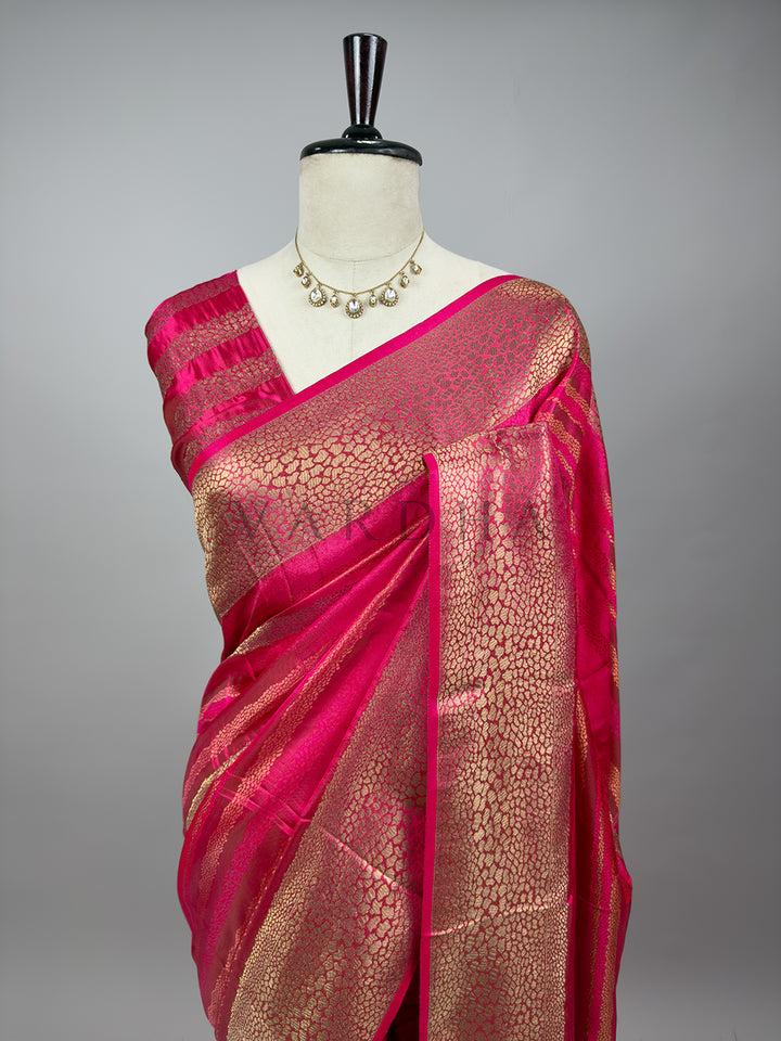 Pink saree with gold patterns on a mannequin against a gray background Upper drape of a Rani Pink Tanchoi Silk Saree on a mannequin paired with a traditional necklace, showcasing the shoulder pleats and intricate weaving patterns.


