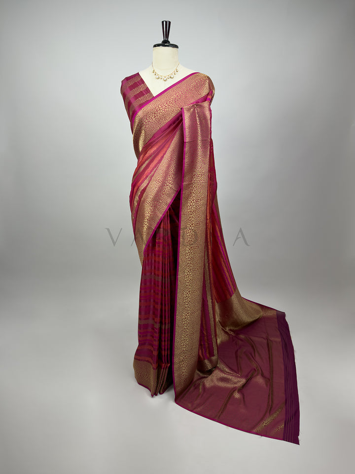 Wine saree with gold border on a mannequin against a gray background A full-length drape of an Exquisite Wine Tanchoi Silk Saree on a mannequin with a delicate kundan necklace. The saree features intricate thread weaving of dense gold and bronze floral patterns beautifully contrasted against a deep wine-purple silk background. The elegant pallu flows gracefully to the floor, displaying the grand composition and royal look of this handwoven ethnic bridal wear.