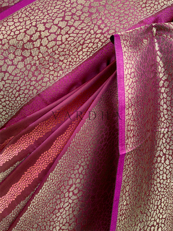Close-up of pink fabric with intricate pattern, likely a sari or similar garment. An extreme close-up detail of the Wine Tanchoi Silk Saree fabric, showcasing the fine texture and high-quality craftsmanship of the intricate handloom weaving. The shot reveals dense patterns of gold and copper threads forming organic, embossed motifs against the smooth wine-colored silk base, highlighting its luxurious premium feel.