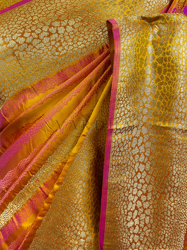 A detailed half-torso view of the draped Yellow Tanchoi Silk Saree on a mannequin, highlighting the exquisite pattern layout across the chest and shoulder drape. The intricate gold and yellow weaving creates a textured, metallic finish, accentuated by vibrant pink borders. A traditional kundan statement necklace complements the ensemble, showing how the luxury fabric frames a formal wedding look. Close-up of a fabric with gold and pink patterns