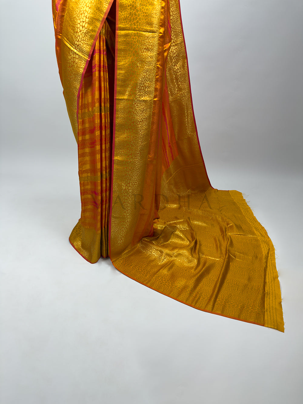 A lower-body perspective focusing on the perfectly aligned front pleats and the structured side drape of the Yellow Tanchoi Silk Saree. The vertical sections show intricate golden geometric and floral weaving patterns, framed by a striking hot pink selvedge. The heavy pallu pools on the floor, accentuating the elegant drape and majestic silhouette of traditional Indian festive attire. Gold saree with a red border on a white background