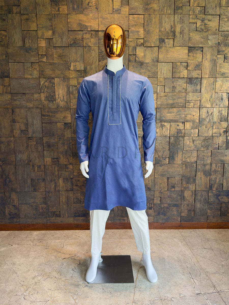 Mannequin wearing a blue kurta against a wooden paneled wall. Close-up of a designer French Blue kurta showing the concealed button placket, central vertical pintuck detailing, and a contrasting rectangular stitched border.