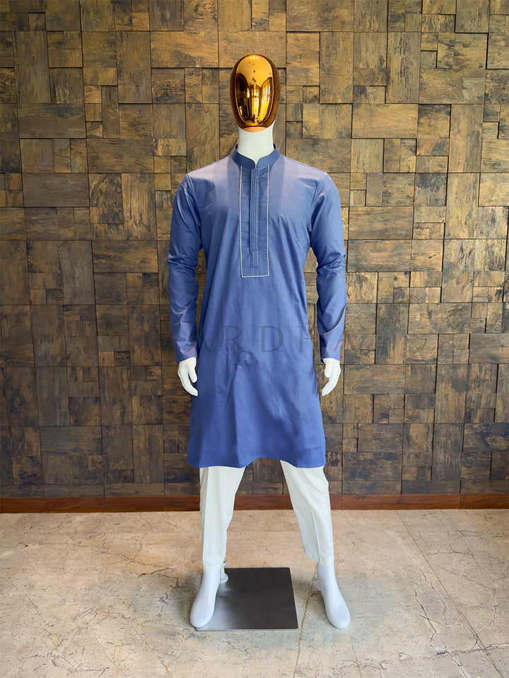 Mannequin wearing a blue kurta against a wooden paneled wall. Close-up of a designer French Blue kurta showing the concealed button placket, central vertical pintuck detailing, and a contrasting rectangular stitched border.