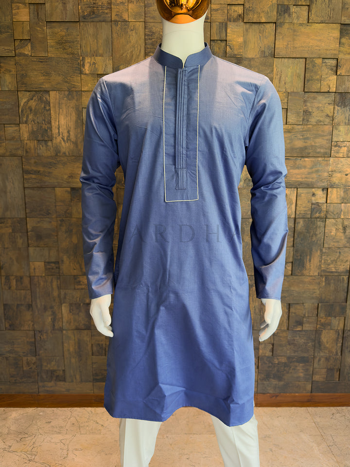 Blue kurta on a mannequin against a wooden paneled wall. Minimalist French Blue designer kurta for men featuring sharp lines, full sleeves, and a formal structured placket without heavy embellishments.