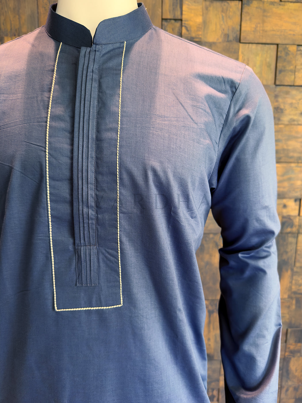 Blue kurta on a mannequin against a wooden background. Steel Blue cotton kurta with a Mandarin collar, styled for a refined ethnic look; recommended to be paired with white or cream pyjamas.