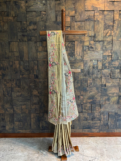 Gold Kanjivaram tissue silk saree with intricate floral embroidery and peacock motifs on the border and pallu.