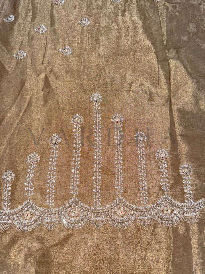 Close-up of a decorative fabric with intricate silver embroidery on a brown background.