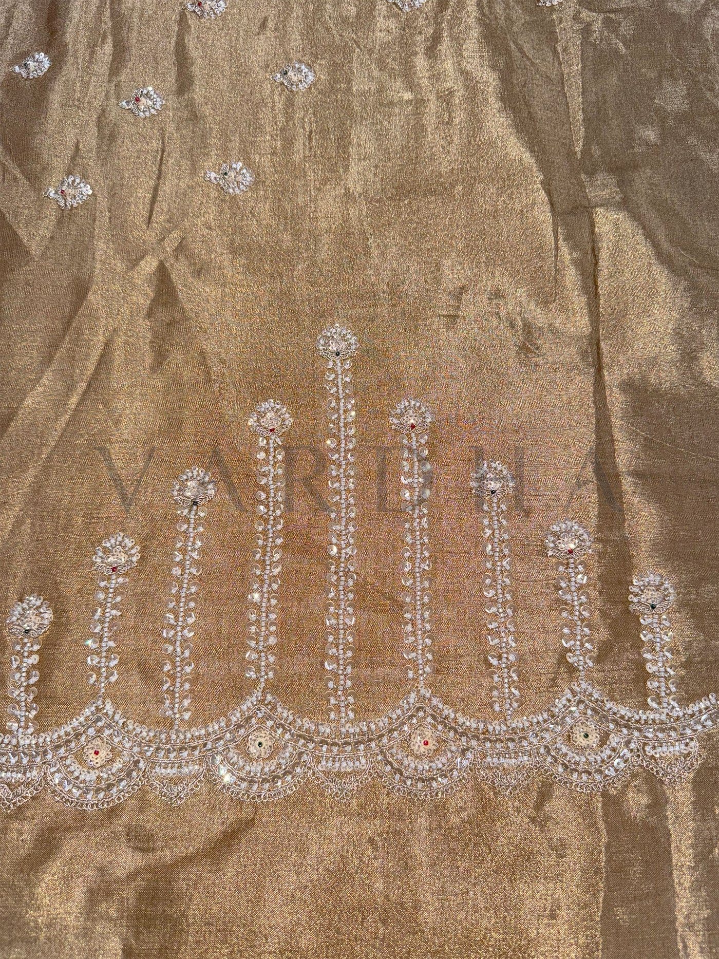 Close-up of a decorative fabric with intricate silver embroidery on a brown background.